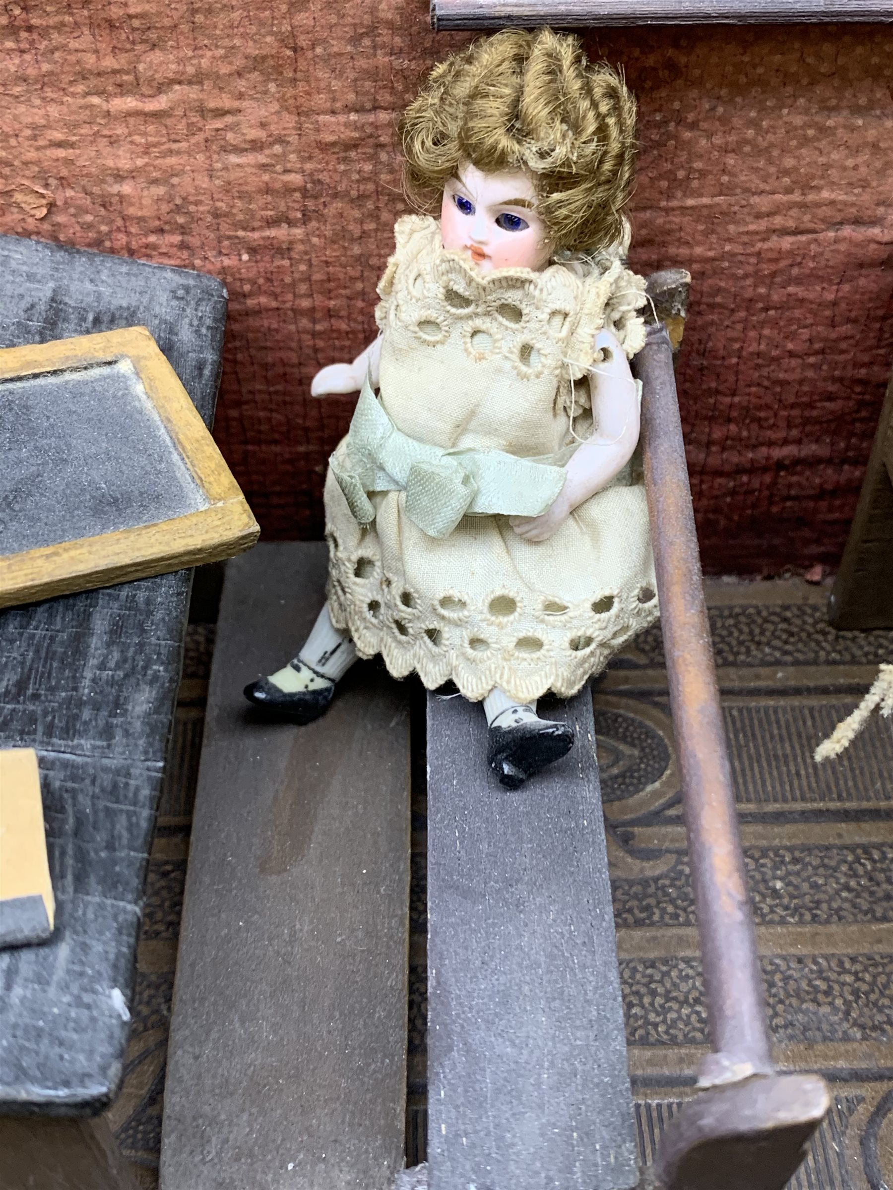 Late Victorian wooden school room setting with bisque head teacher and six German all bisque pupils each seated at a combined desk and chair with slate board, in a classroom furnished with chest of drawers, fire-surround, lectern, wall map, pictures, miniature books, school bell, chalk board on easel, wall clock etc, L70cm H28cm D28cm