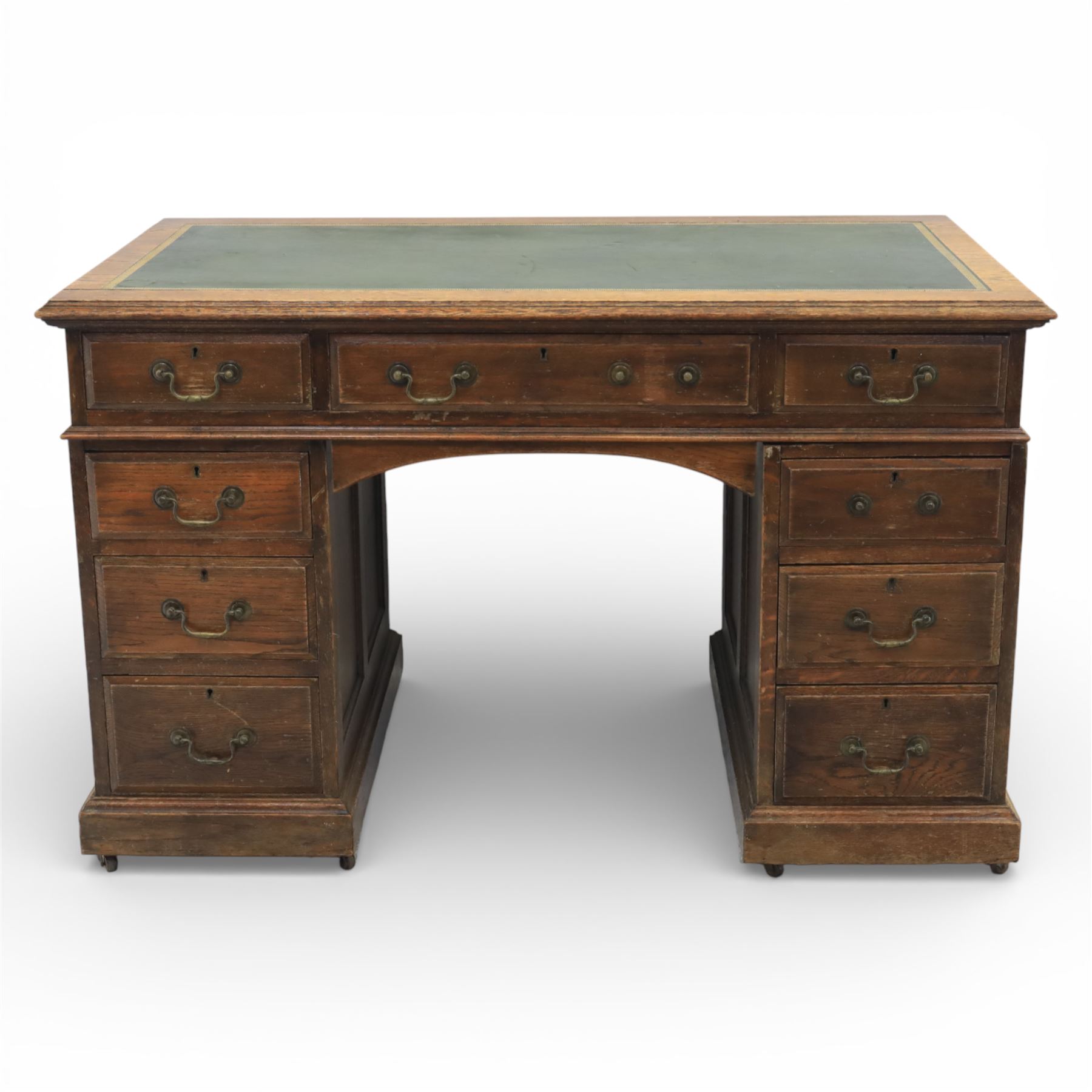 Victorian oak pedestal desk, the rectangular top with inset green leather writing panel and decorative gilt border, over a central frieze drawer flanked by two short drawers, twin pedestals each fitted with four drawers with brass handles, arched kneehole opening, standing on moulded plinth bases