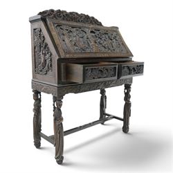 Early 20th century Chinese export carved hardwood writing bureau, the sloped fall front deeply carved with a narrative figural scene beneath pine and prunus trees, above a pair of rectangular carved panels, the shaped crest rail with entwined dragons, interior fitted with pigeonholes and a central drawer, on figural front supports with shaped stretcher