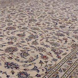 Central Persian Kashan hand-knotted carpet, ivory field densely decorated with an all-over design of scrolling floral vines and palmettes, framed by multiple borders with continuous floral meander and rosette motifs, in a palette of indigo, ivory, soft blue, sage green, rose and ochre tones, with cotton fringe ends 