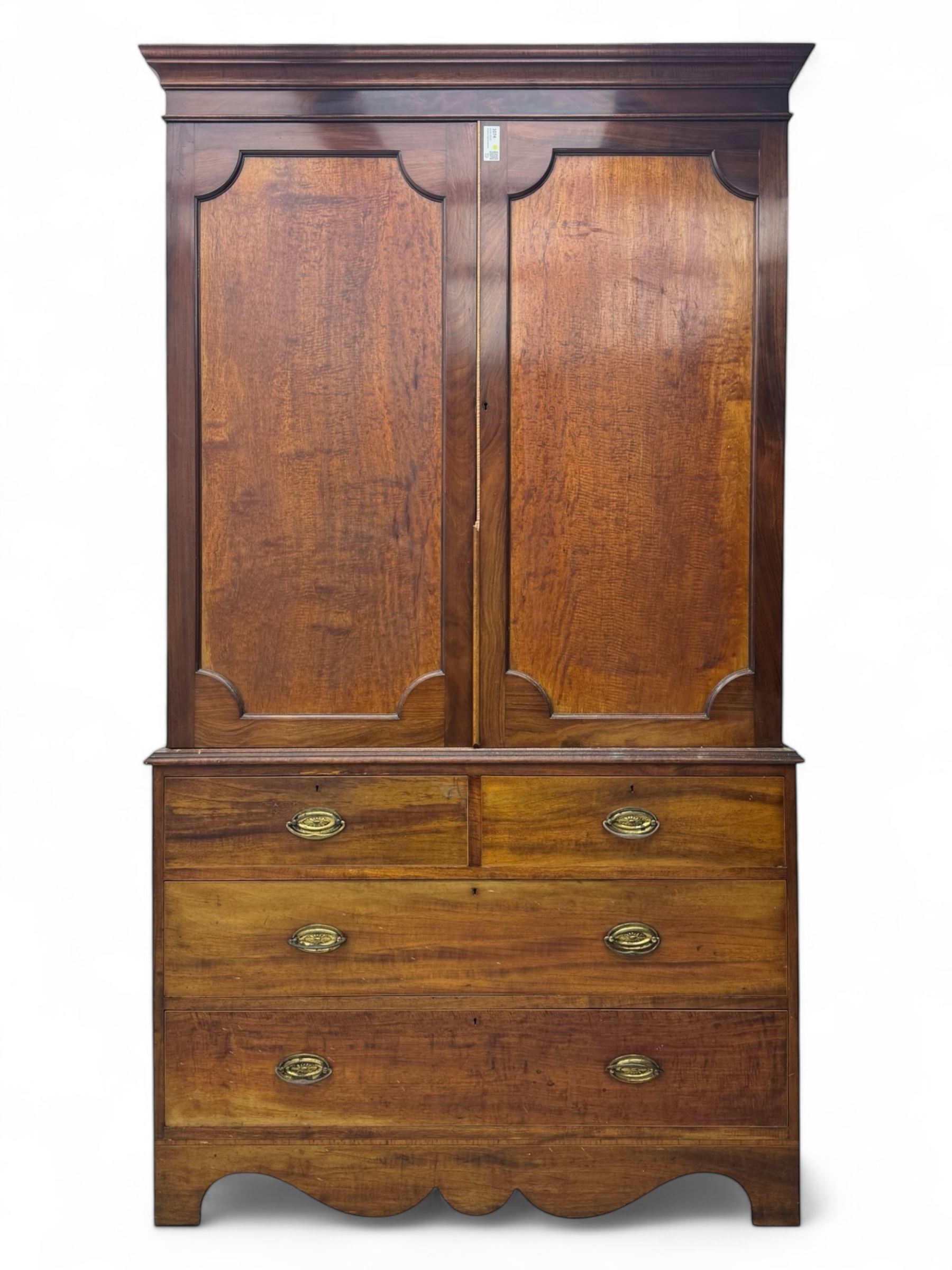 George III mahogany linen press cupboard, projecting moulded cornice over two panelled doors, the interior fitted with two slides and shelf, two short and two long drawers below, shaped apron over bracket feet 