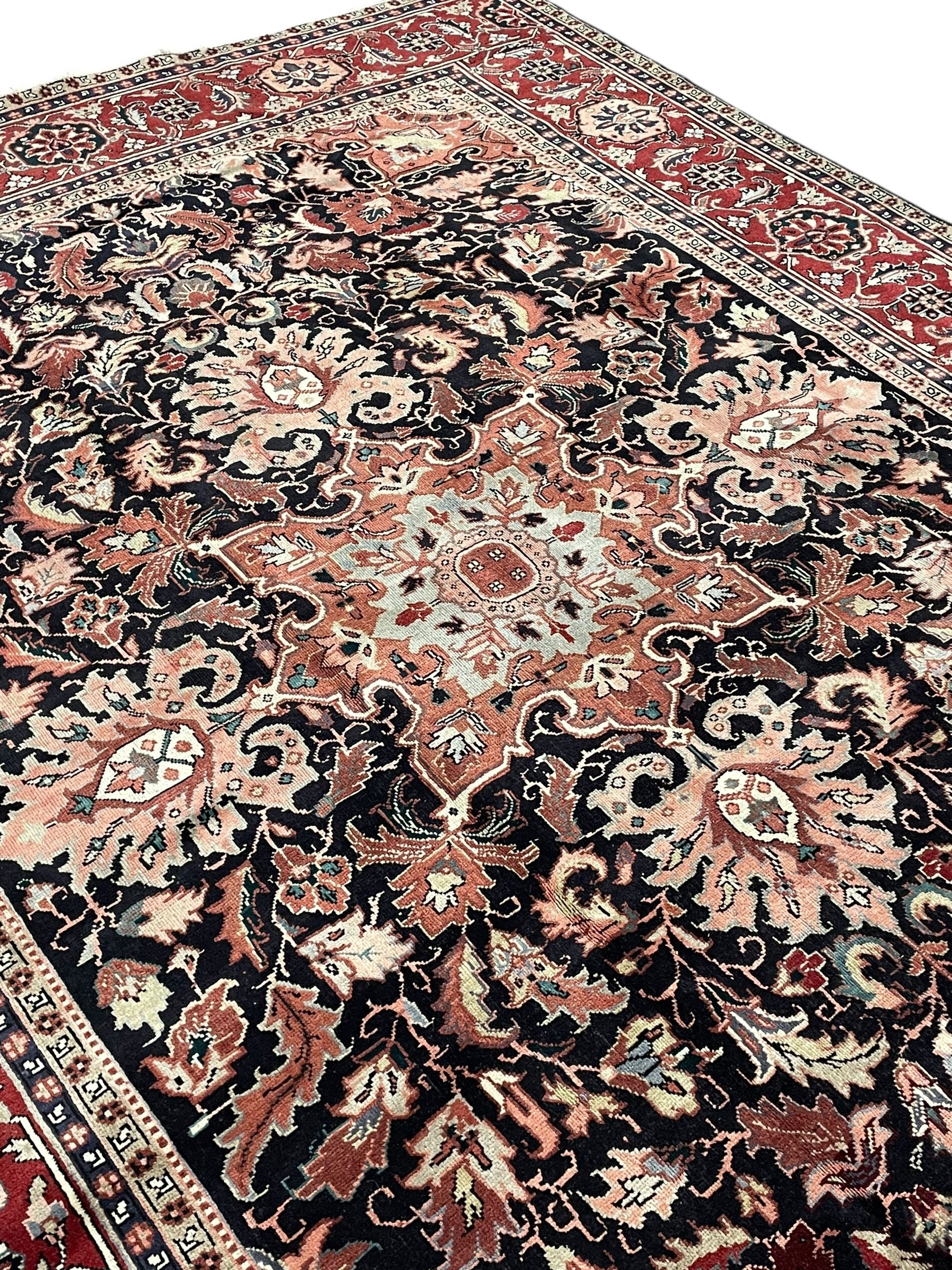 Persian Heriz dark indigo and red ground carpet, the central medallion with large projecting palmette motifs, overall floral design decorated with stylised plant motifs, repeating patterned border within guard stripes