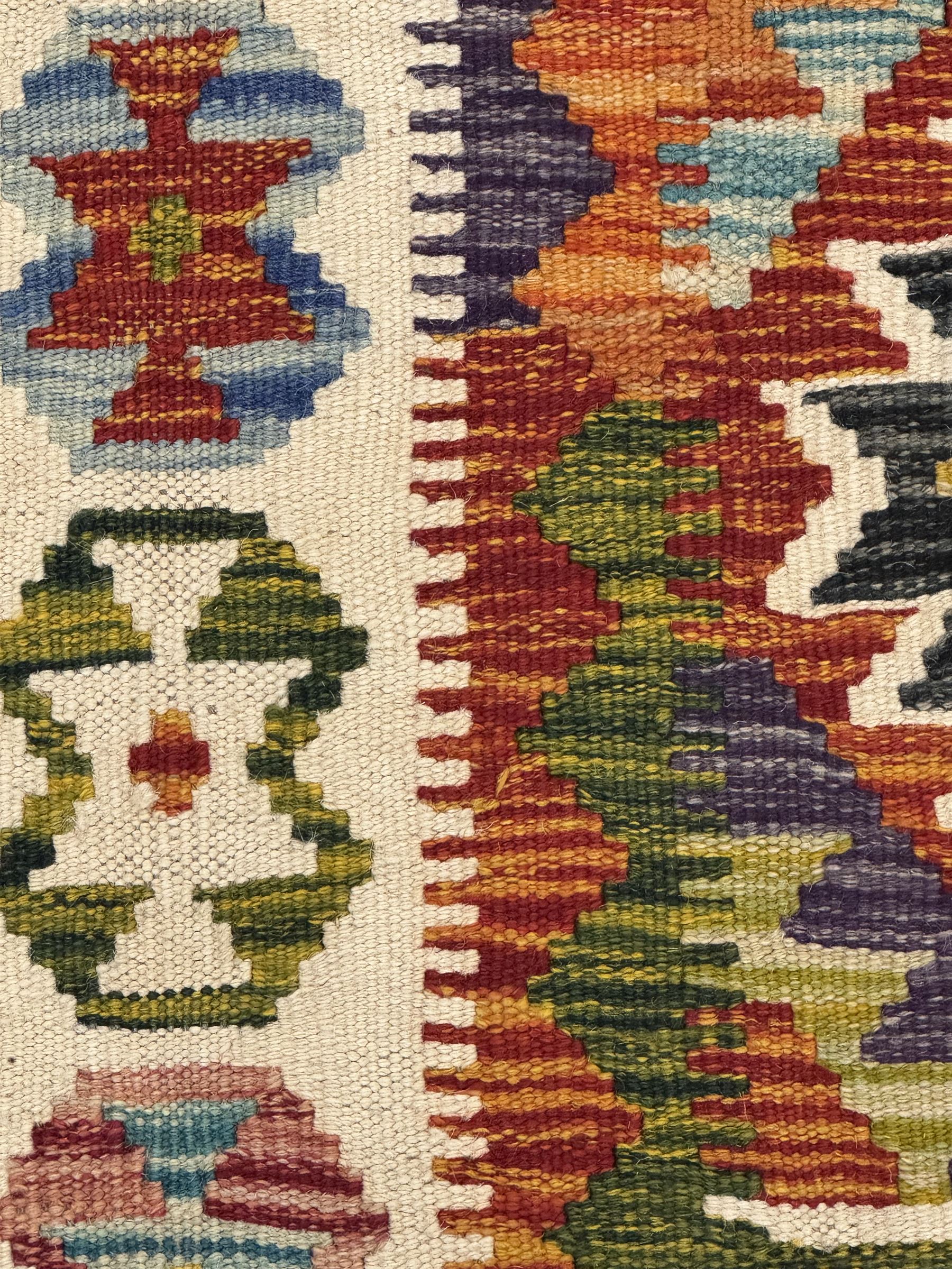 Chobi Kilim flatweave rug, cream ground with a multicoloured geometric diamond field, framed by a bold border of repeating stylised motifs, finished with braided corner tassels