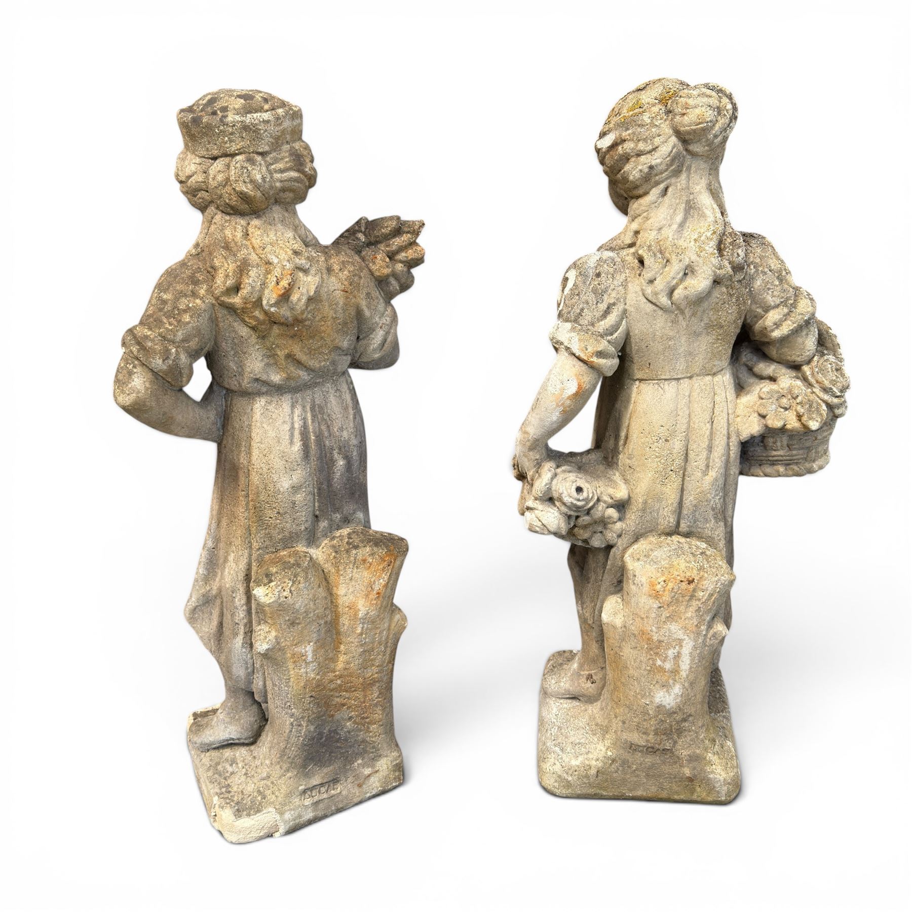 Lucas Stone - pair of cast stone garden figures, modelled as young female figures holding wheat sheafs and baskets of flowers, each on square bases, weathered finish, makers mark stamped to base