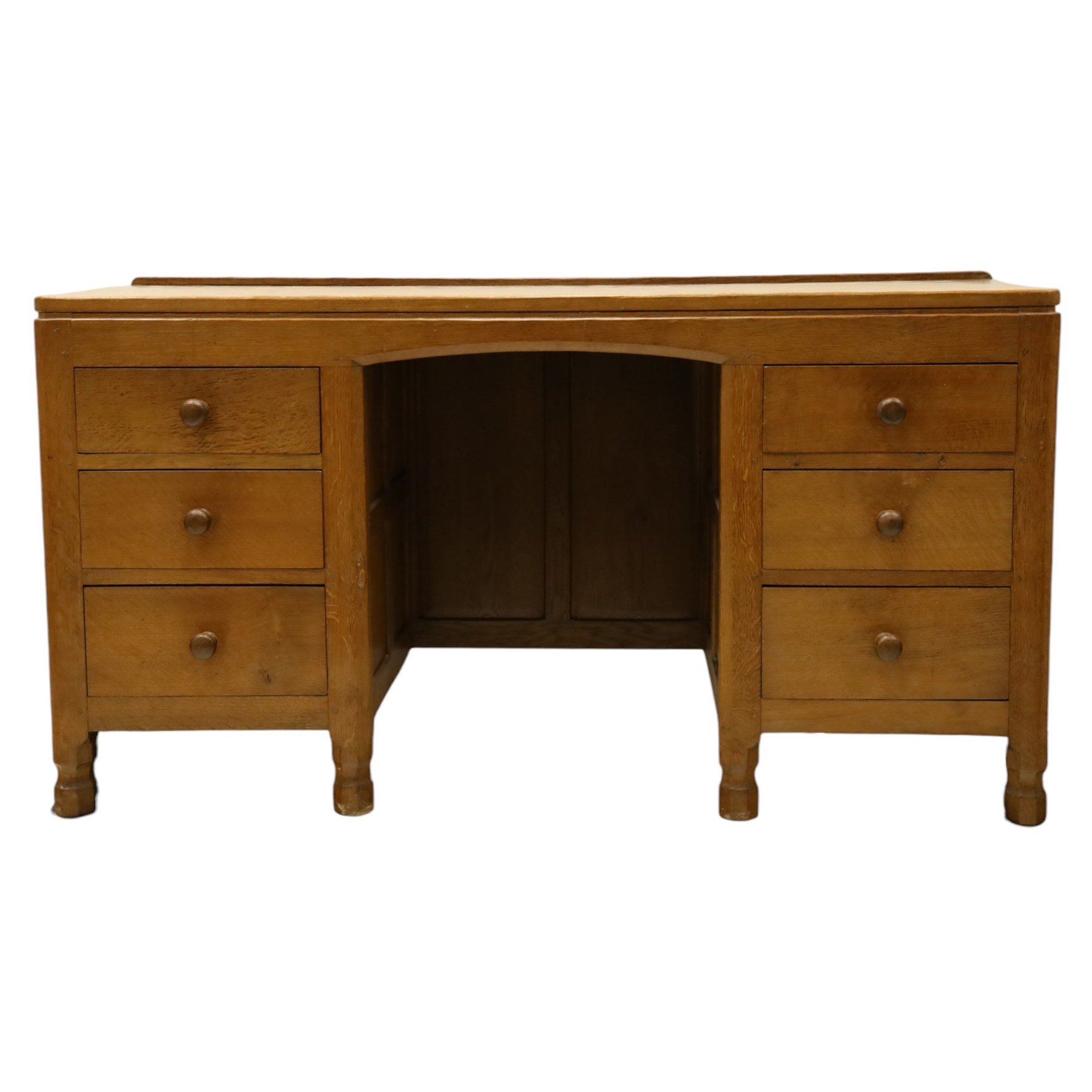 Mouseman - adzed oak kneehole dressing table or desk, the rectangular adzed top with raised back and canted corners, over an arched recessed kneehole flanked by three graduating drawers to each side with turned knob handles, raised on octagonal feet, with carved mouse signature, by the workshop of Robert Thompson of Kilburn