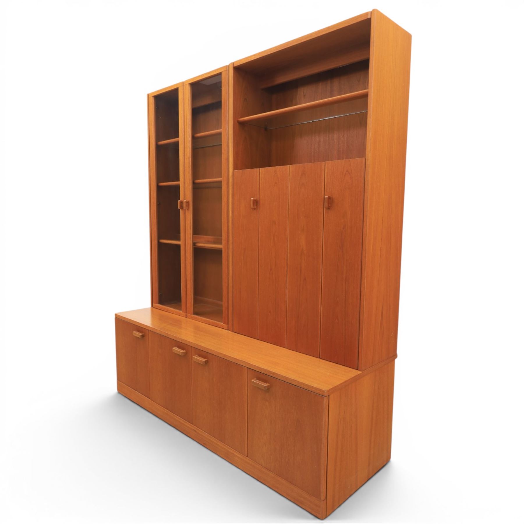 G-Plan - Mid 20th century teak modular wall unit, the upper section fitted with twin glazed doors enclosing shelves, adjoining concertina doors with mirrored and shelved interior, the base with four cupboard doors with recessed rectangular handles, raised on a plinth base