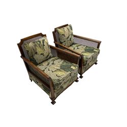 Early 20th century bergère lounge suite, mahogany framed with cane work back and sides, acanthus scroll carved uprights - three seat sofa (W167cm, H82cm, D83cm), and pair matching armchairs (W78cm), loose cushions upholstered in acanthus leaf scroll fabric with scatter cushions