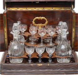 Late 19th century cave à liqueur black forest style decanter box, with carved naturalistic decoration, lifting top and fold out side panels, the interior fitted with four decanters and sixteen glasses, the smaller glasses with applied painted decoration, the others with etched design, with key, when closed overall W36cm x D29cm x H28cm 