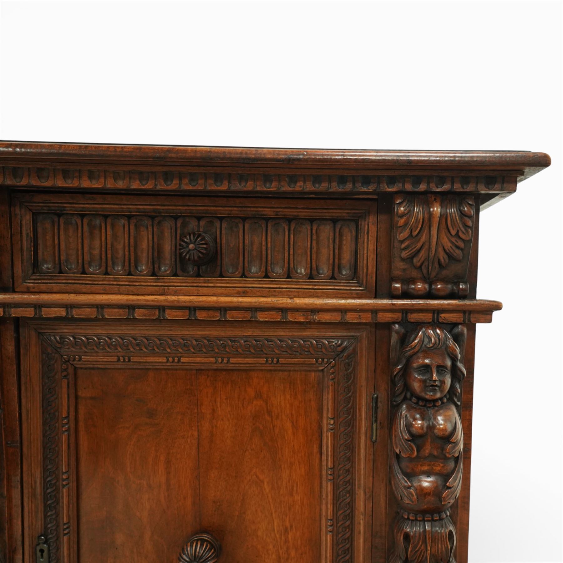 19th century Italian walnut Renaissance Revival side cabinet, the moulded rectangular top above a frieze drawer carved with vertical fluting and a central rosette, with egg-and-dart moulded rails to the top and base, acanthus-carved corbels below, the panelled cupboard door framed by beading and guilloche ornament, flanked by carved caryatids modelled as classical female architectural supports with foliate terminals, raised on paw feet