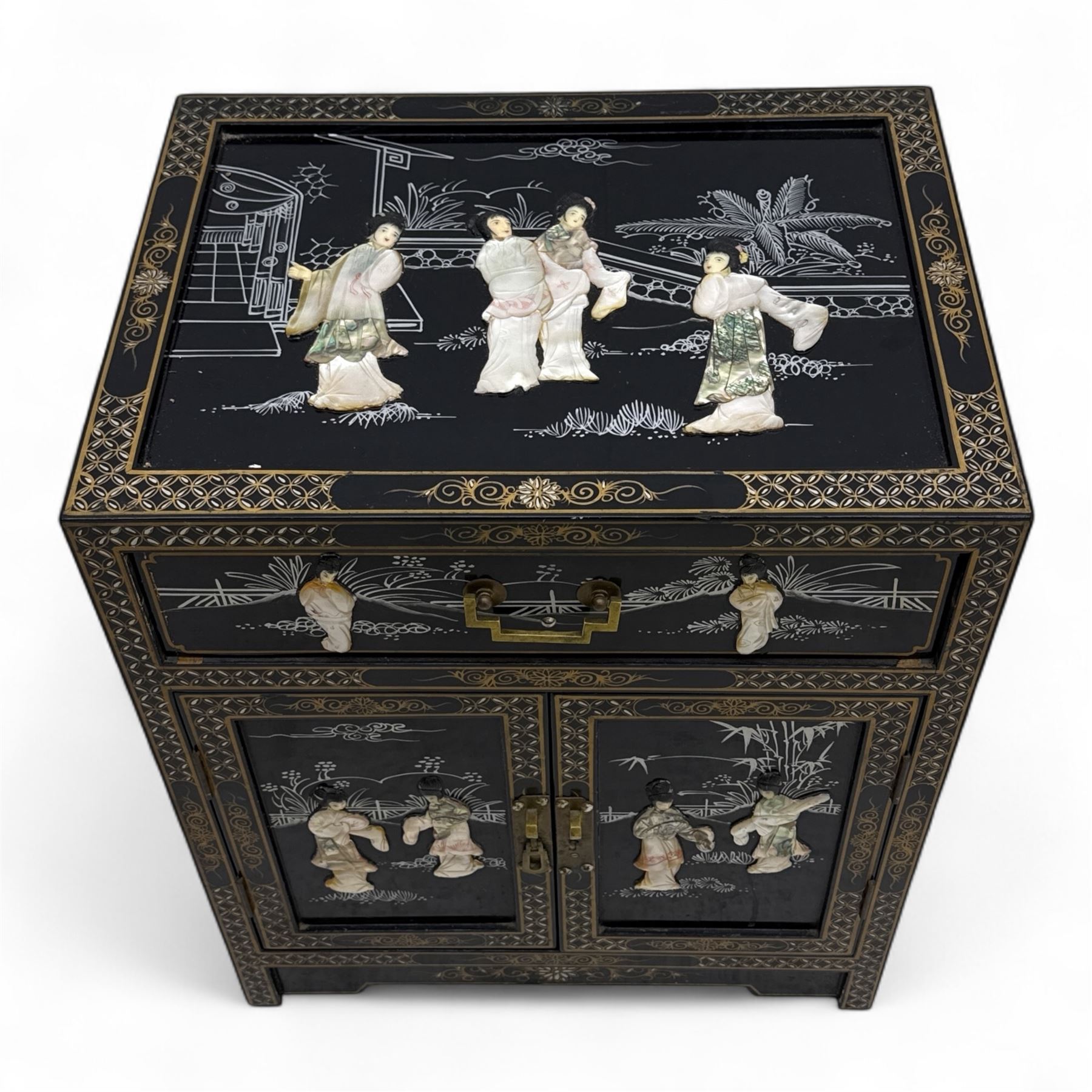 20th century Japanese Shibayama style black lacquered cabinet, rectangular form decorated with mother-of-pearl and hardstone figural inlay, the top with four standing figures, single frieze drawer above two cupboard doors, gilt painted borders and landscape