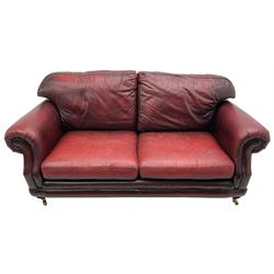 Thomas Lloyd - three-piece lounge suite, comprising of traditional shape two seat sofa (W190cm H80cm) and a pair of wingback armchairs (W100cm H91cm), each with rolled arms over turned supports with brass castors, upholstered in oxblood red leather