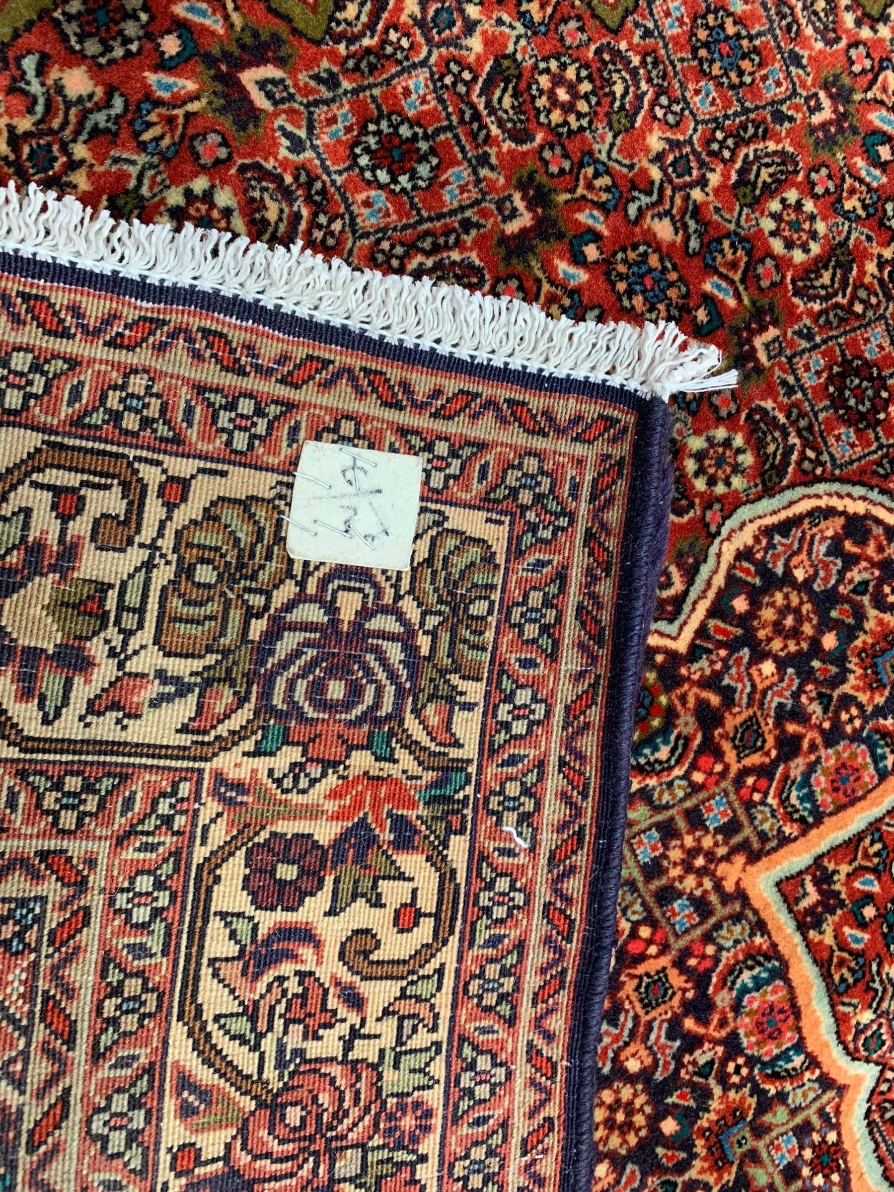 Persian Bidjar crimson ground rug, thick woollen pile, the field decorated with repeating Herati motifs within cusped outlines, the guarded border decorated with repeating flower head motifs