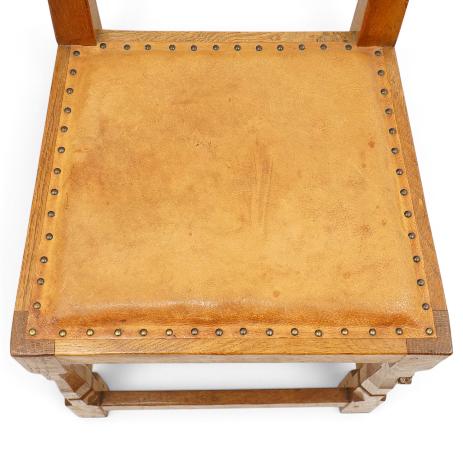 Mouseman - set of six (5+1) 1940s pre-war panel-back dining chairs, the raised backs with adzed panels, over seats upholstered in tan leather with studwork border, raised on octagonal turned baluster supports united by box stretcher, with carved mouse signature, by the workshop of Robert Thompson of Kilburn

Provenance: ordered directly from the Mouseman workshop in the 1940s before the outbreak of the war, the items were subsequently delivered after the end of war. 