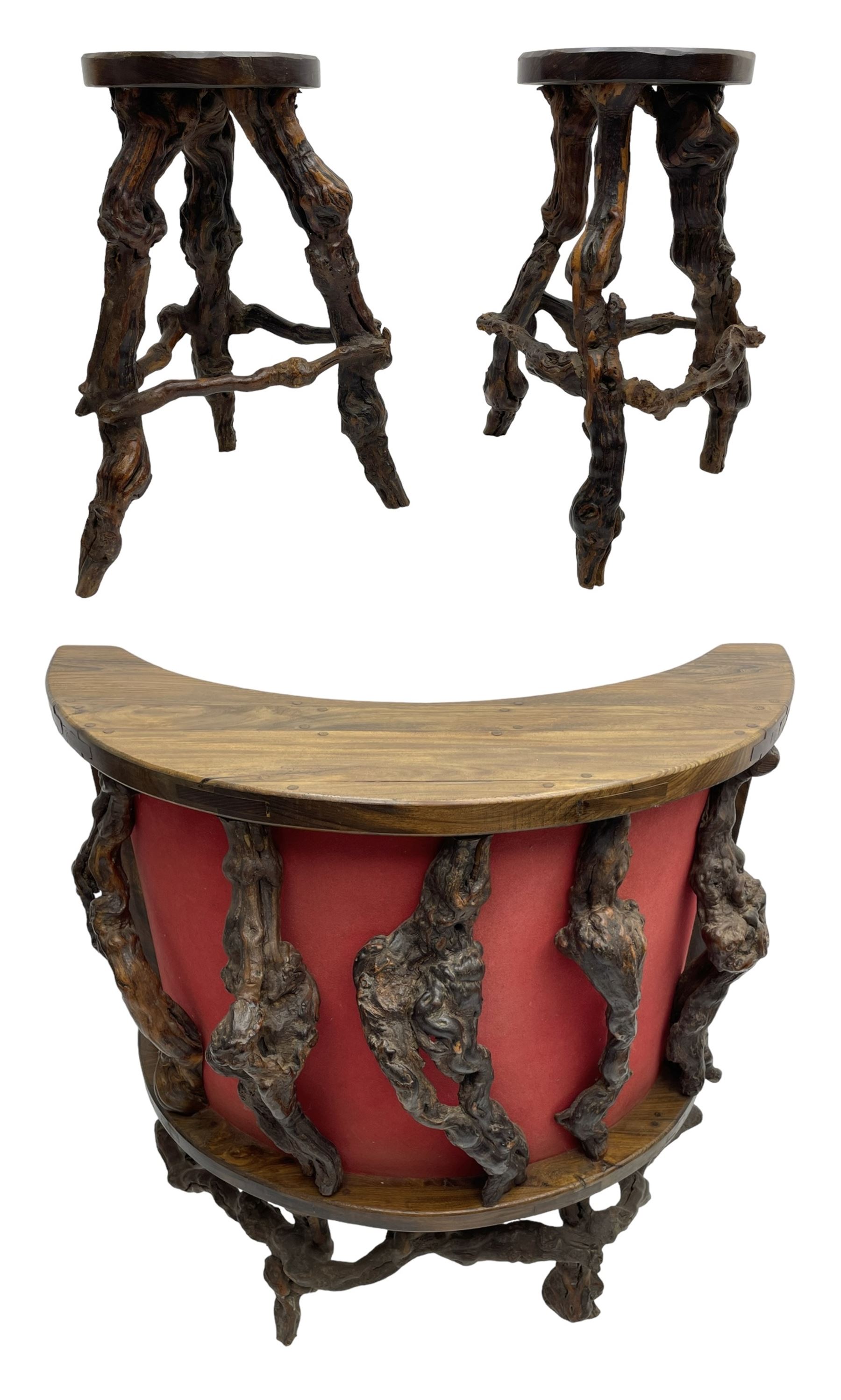 Mid-20th century French grapevine and walnut bow-front wine tasting bar, the curved counter top supported by sculptural grapevine roots, fitted with single shelf and raised on rustic vine feet (W100cm H101cm); with a pair of matching bar stools, the circular top raised on three gnarled root supports united by stretchers (W50cm H70cm)