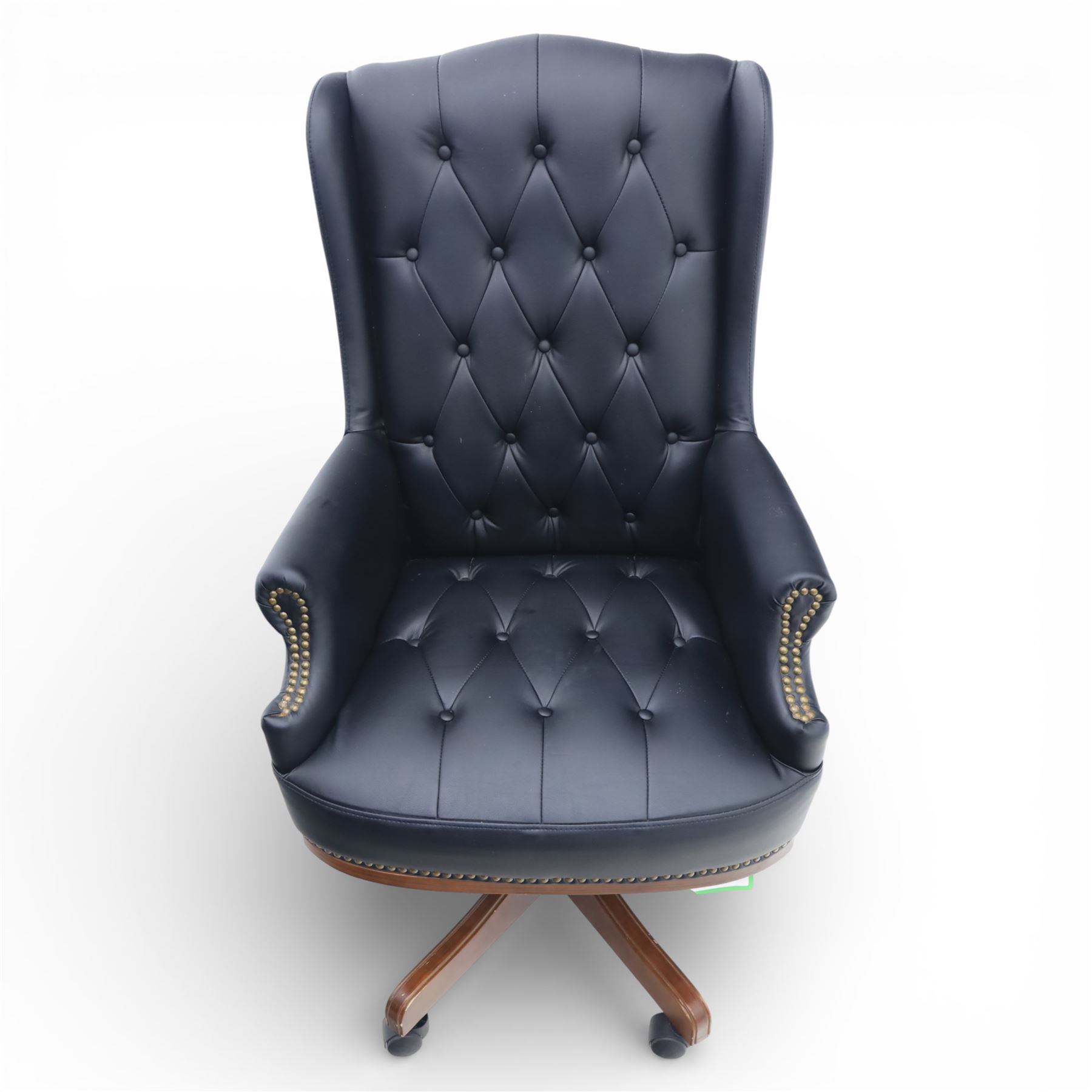 Chesterfield style desk chair upholstered in black, brass studded trim with tall button backed seat, with faux wooden base raised upon castors