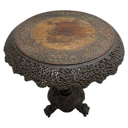 Late 19th century Anglo-Indian carved hardwood occasional table, circular tilt-top carved profusely with mythical animals and foliage decoration, pierced and carved with interlaced leafy branches, leaf carved pedestal supports on a raised platform with further carved and pierced foliage decoration, four carved feet in the form of mythical beasts with gaping jaws 