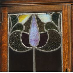 Arts and Crafts oak dresser, projecting moulded cornice above three glazed panels with coloured leaded glass floral panels, flanked by two glazed doors enclosing two adjustable shelves, open mirrored recess below with mirrored back, the base fitted with two short drawers over two central drawers flanked by carved panelled cupboard doors, ornate brass handles, raised on tapering square legs