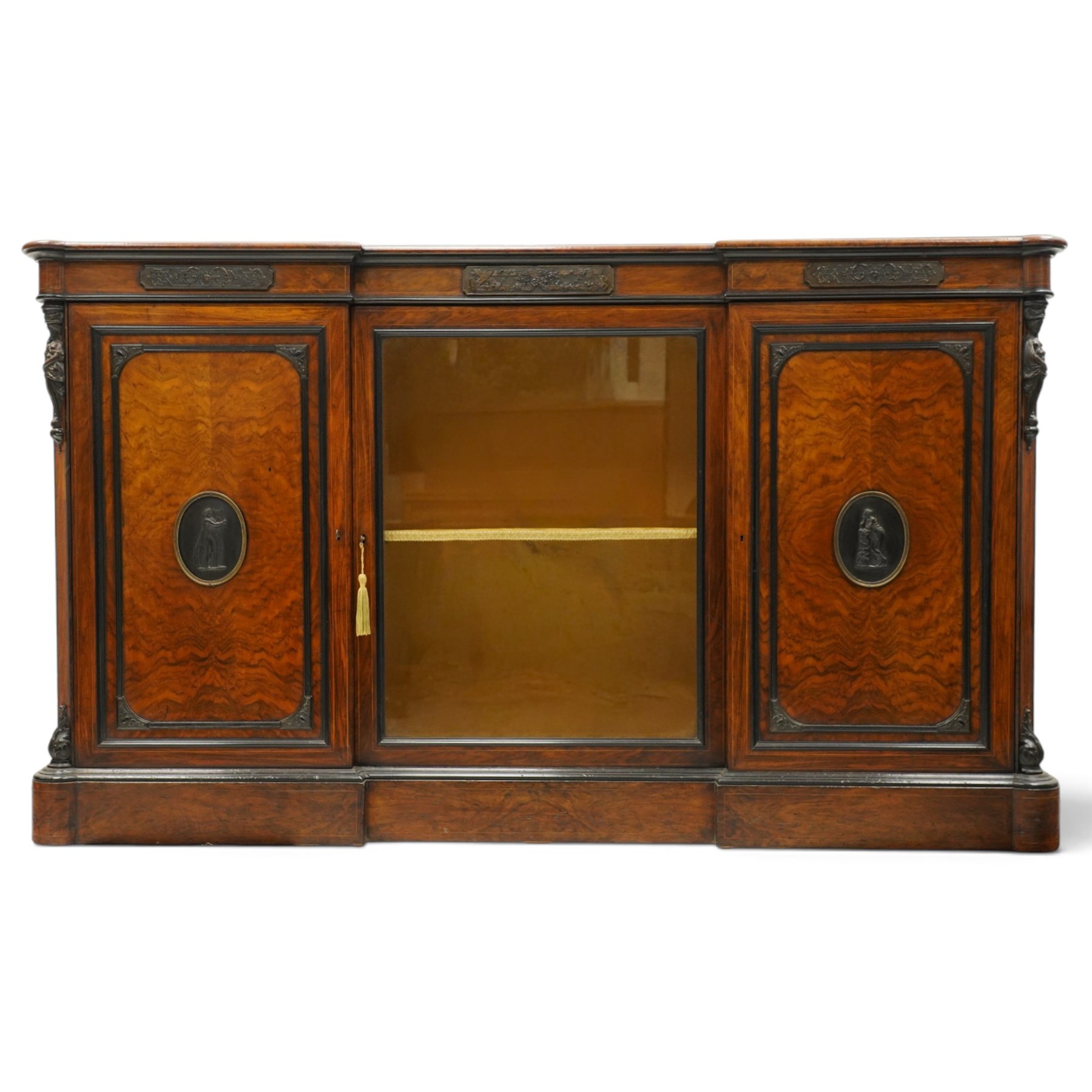 Lamb of Manchester (est. 1843) - Victorian Aesthetic Movement inlaid figured and burr walnut inverted-breakfront credenza, the shaped rectangular top with ebony banding and boxwood stringing, the frieze applied with bronze mounts decorated with foliate and scroll motifs, fitted with central glazed door flanked by panelled doors with central oval metal plaques depicting Classical Muses with lyre, the flanking canted uprights applied with caryatid maidens holding torches, acanthus terminal over skirted base