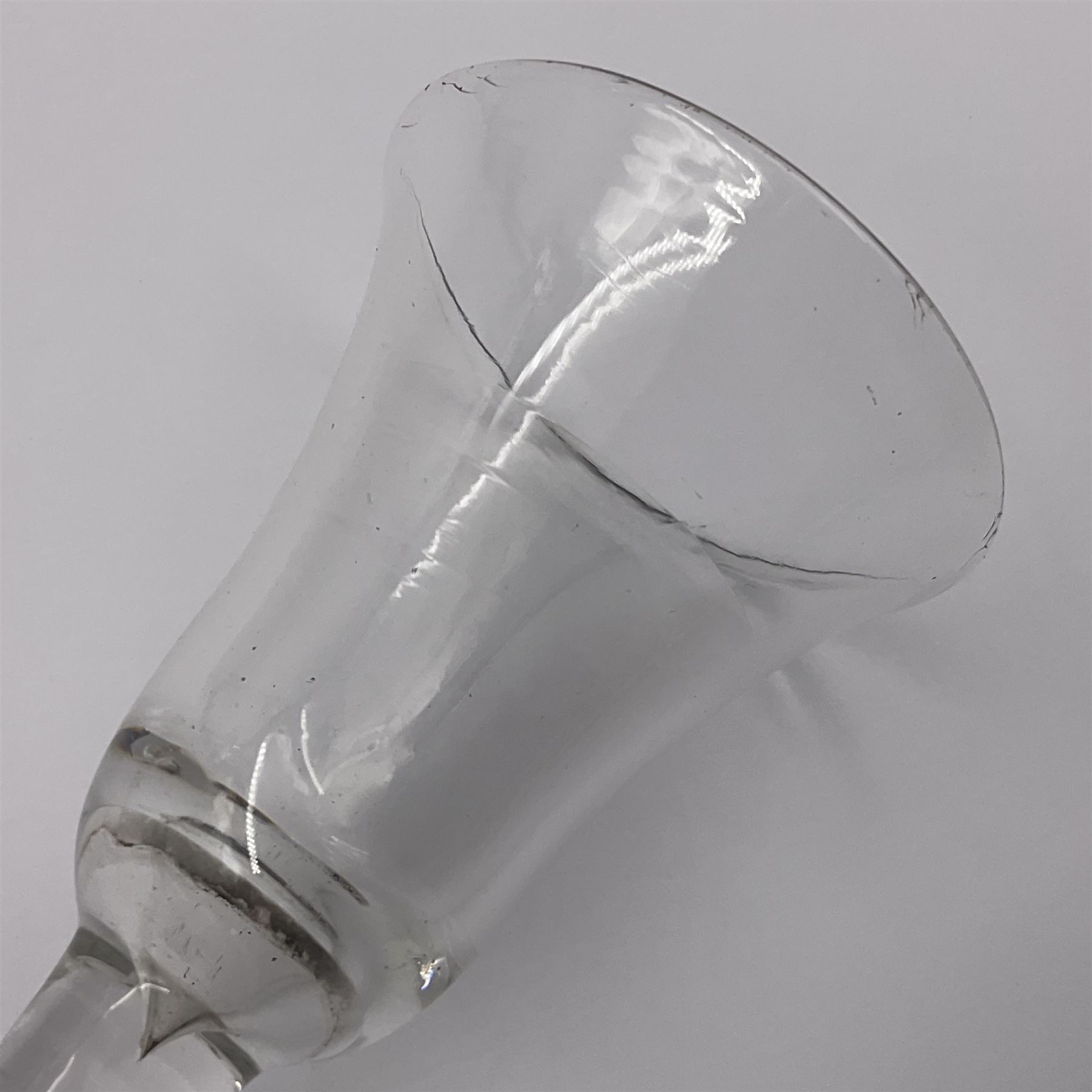 Three 18th century wine glasses comprising a plain stemmed glass with bell shaped bowl and conical folded foot H16cm, another plain stemmed glass with ogee bowl and folded foot and a Continental glass with gilt faceted bowl, decorated with male figure within a landscape, on a clear Silesian seven sided cut stem (3)