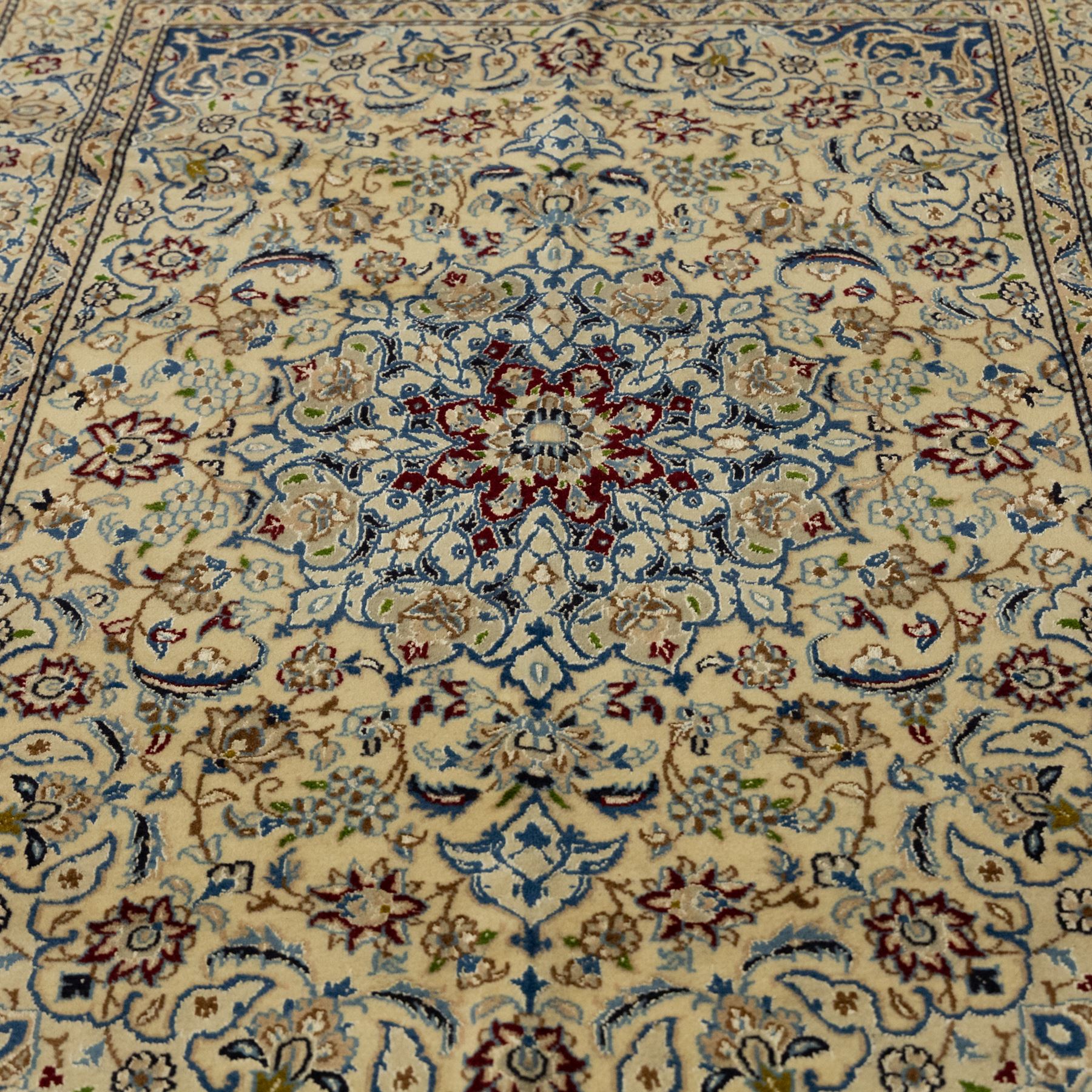 Central Persian fine Nain hand-knotted rug, ivory ground, with a central shaped floral medallion with pendants, surrounded by scrolling foliate and floral motifs incorporating rosettes, palmettes and delicate vine work in blue, cream and beige tones, enclosed by blue spandrels and an ivory border with repeating palmettes and meandering vines, flanked by floral guard stripes, with cotton fringes