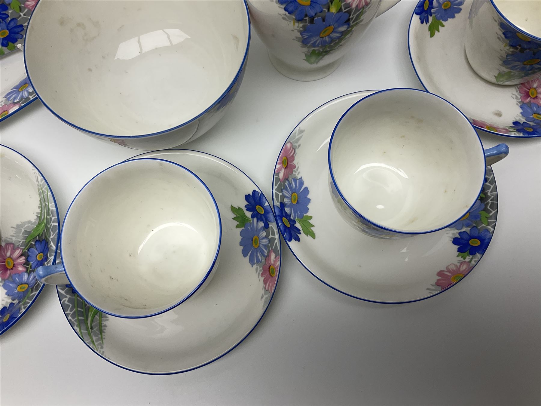 Shelley Strand shaped tea wares, decorated with blue and pink daisies upon a white ground, comprising four teacups, four saucers, three tea plates, milk jug, sugar bowl and cake plate, all with printed green mark beneath and painted pattern no 12216