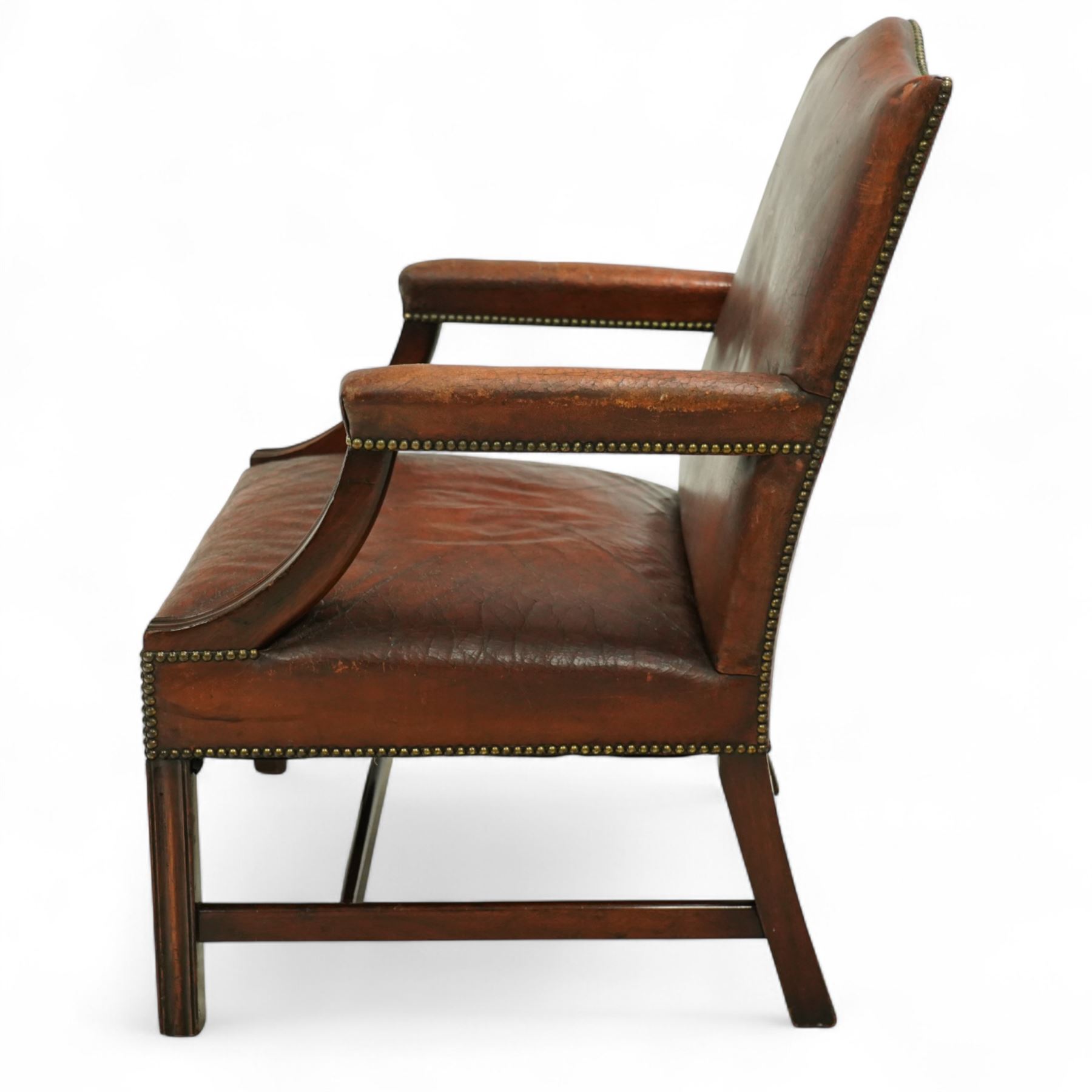 Early 20th-century Gainsborough-style library armchair, padded back, arms, and seat, brass button upholstered in brown leather, on square tapered front legs united by a stretcher 