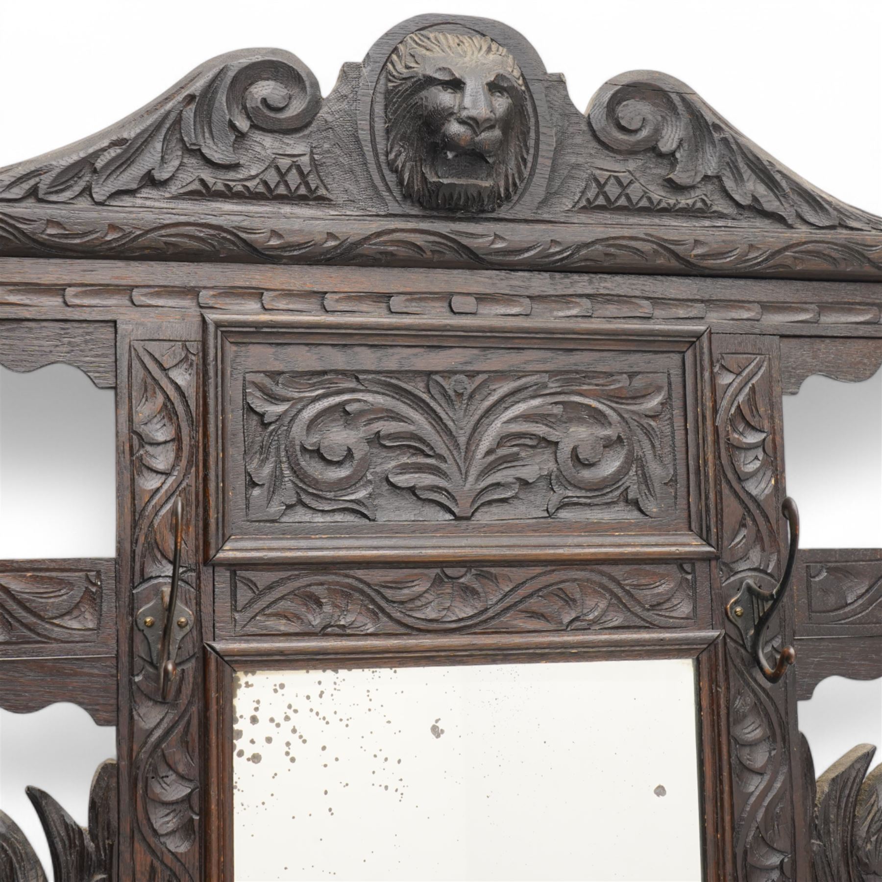 Late Victorian heavily carved oak hall stand, the scrollwork pediment with carved lion's head, bevelled mirror plate flanked by carved dragon motifs, over hinged storage compartment and umbrella stands with drip trays, on turned front supports