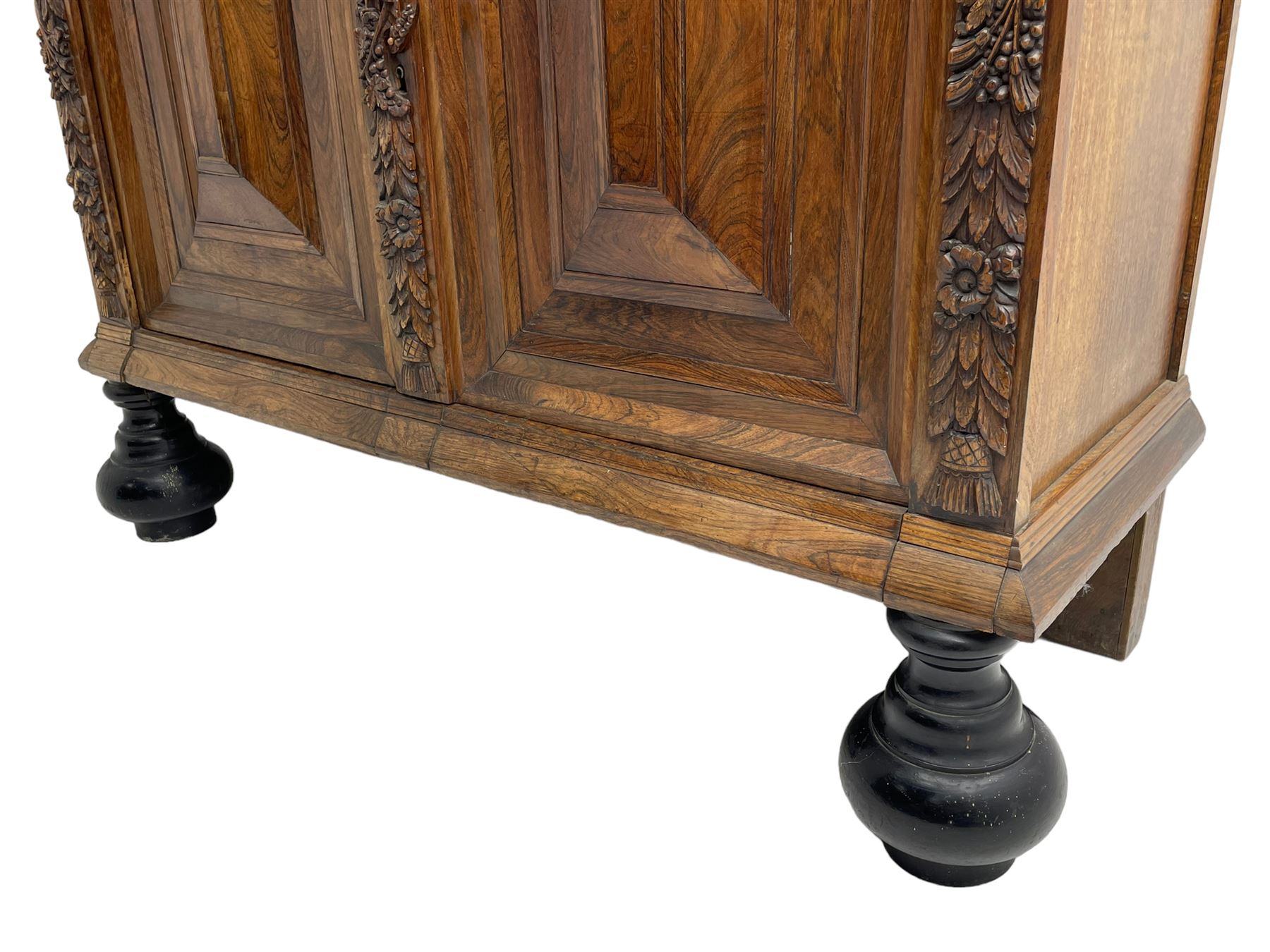 Late 17th century Flemish/Dutch rosewood and oak ‘Zeeuwse Kast’ or cupboard, projecting cornice carved with three putti masks, the uprights carved with lion masks over ribbons, flower heads and foliage, enclosed by four geometric panelled doors, lower central upright carved with flower head over foliate ribbon with bird among foliage, the escutcheon hidden by swivel berry carved cover, interior fitted with shelves, two drawers and shallow hinged cupboard, on two large turned and ebonised feet, circa 1680