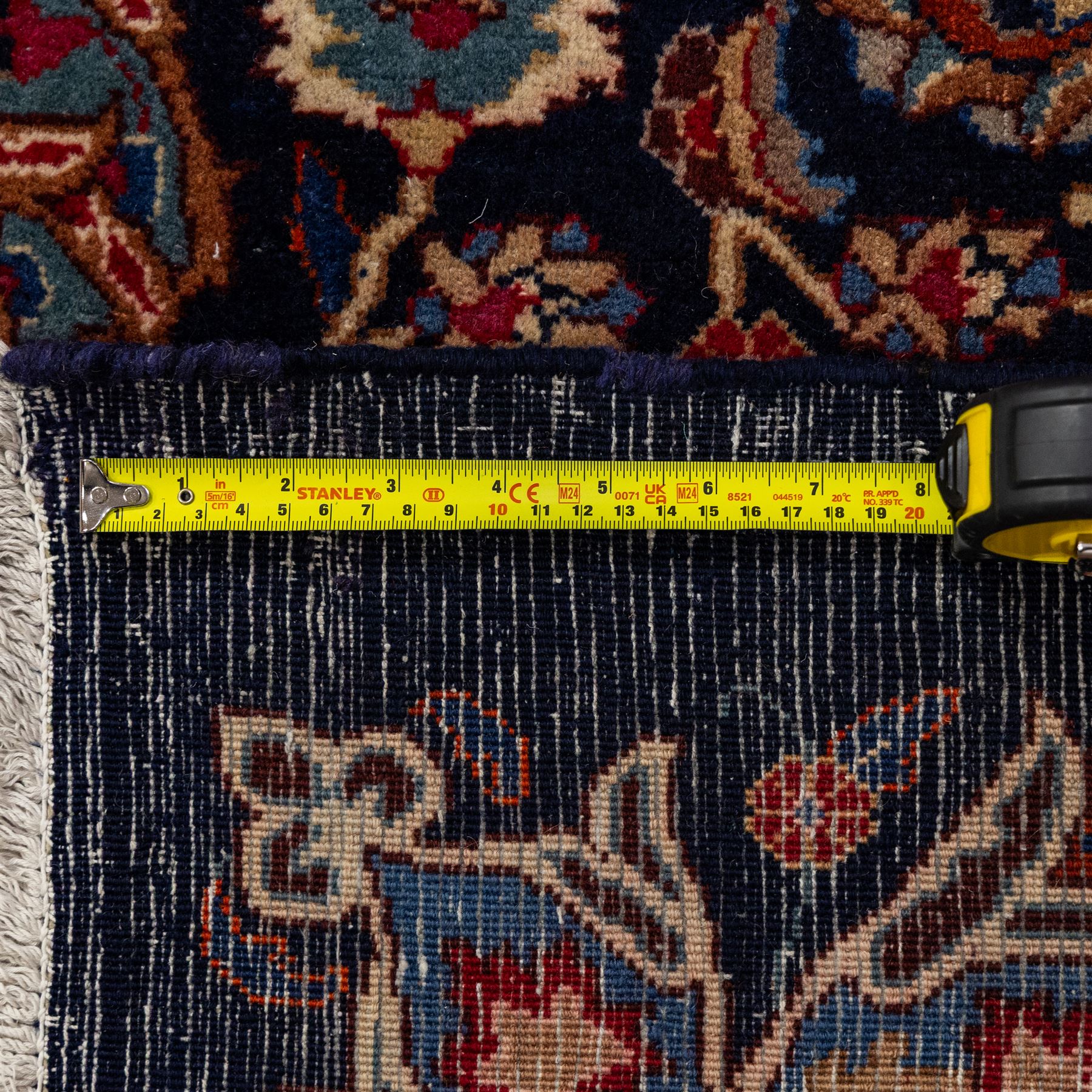 North East Persian Meshed hand-knotted carpet, deep navy field with central complex medallion and densely decorated scrolling floral sprays and palmettes, incorporating cartouche motifs enclosed by a broad tan and dark blue border ornamented by stylized vases flanked by multiple guard stripes, signed 'Amal-e Haji translates as the Work of Haji', with cotton fringe ends 