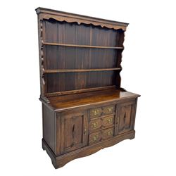 Late 19th century oak dresser, the upper section with two shelves beneath a shaped cornice, the lower section with a central bank of three drawers flanked by cupboard doors, all decorated with geometric diamond motifs, the drawers fitted with brass handles, raised on a shaped plinth base