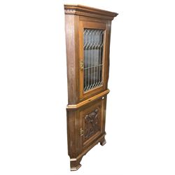 Arts & Crafts period oak corner cabinet, projecting cornice over astragal glazed door and single panelled door decorated with applied carved foliate scrolls and stylised roods surrounded by moulded edge, enclosing single shelf