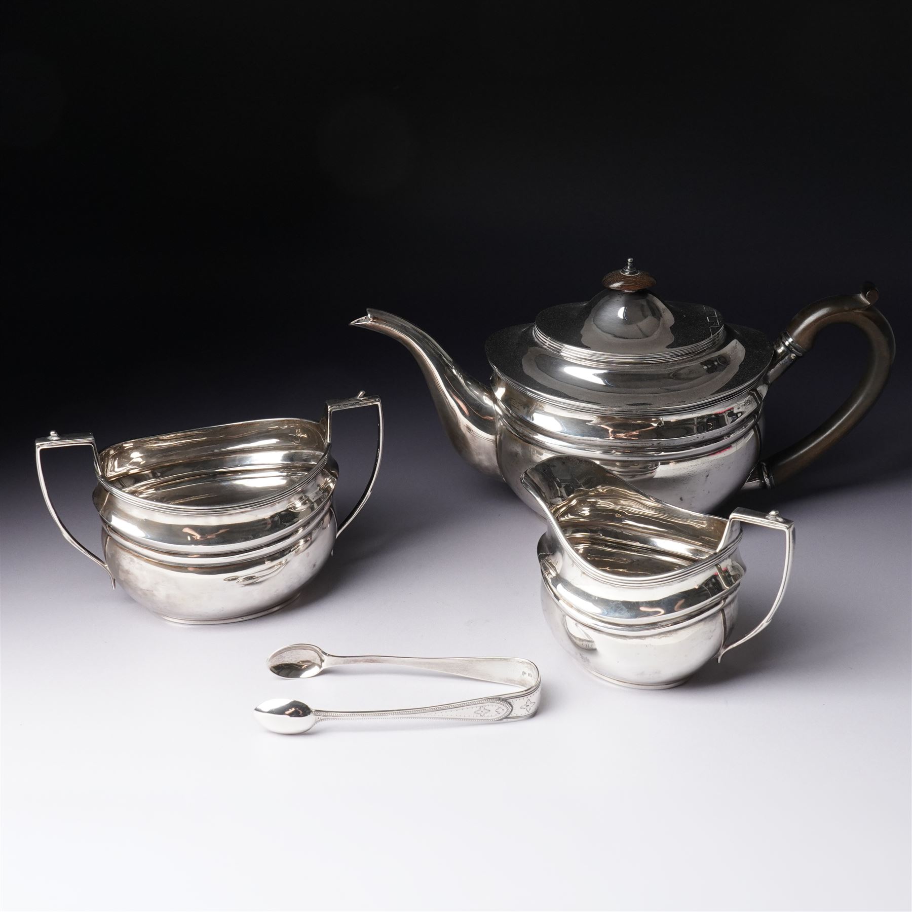 Silver three piece tea set of oval form, the teapot with ebonised handle and lift London 1913 Maker John Hunt and a pair of Victorian silver sugar tongs