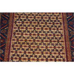 North East Persian Kurdie hand-knotted runner, camel ground with an all-over lattice of rosette motifs linked by angular vines, terminating in a stepped lozenge panel, with a madder red field, spandrels with geometric and zoomorphic devices, indigo main border of angular vines and repeating rosettes, flanked by narrow guard stripes, cotton fringe ends  