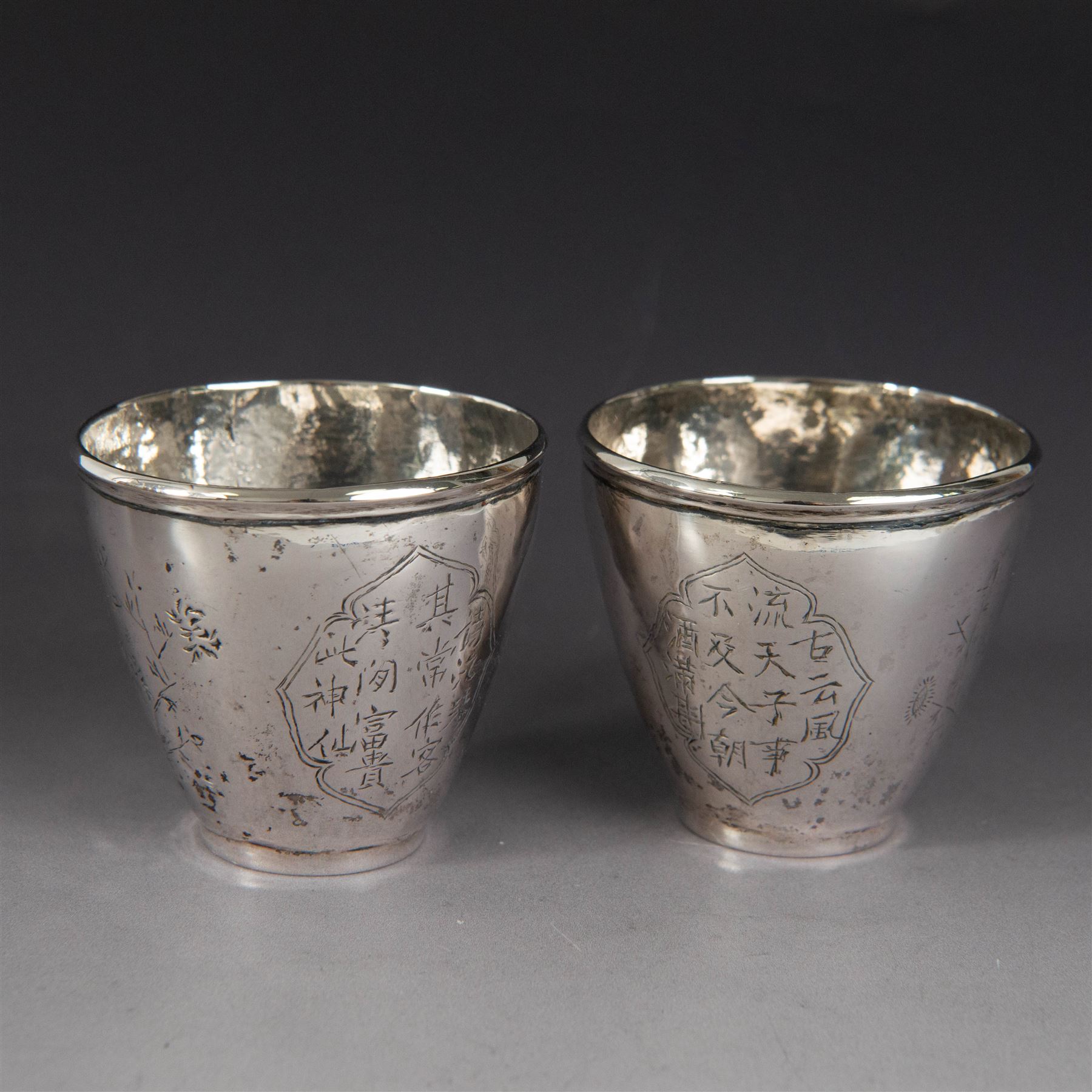 Pair of Chinese export silver teacups, both decorated with character marks, one with floral decoration, the other decorated with a bird within bamboo branches, both with indistinct maker's marks beneath, H6cm