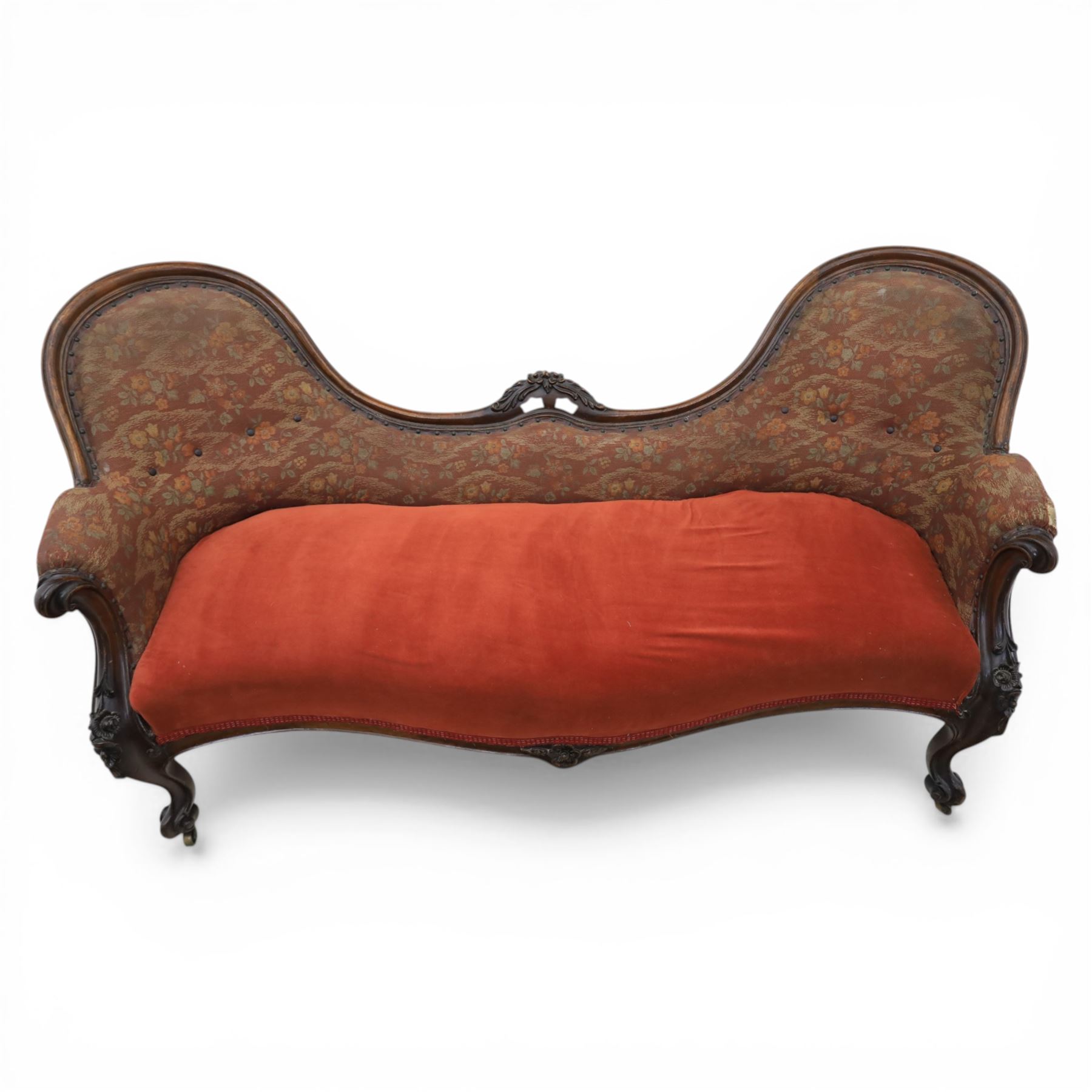 Victorian mahogany framed serpentine sofa, the shaped button upholstered back with central carved foliate cartouche, and scroll arms with carved terminals, over upholstered red seat, upon carved cabriole supports with castors