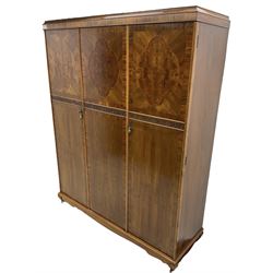 Early 20th century figured walnut triple wardrobe, banded cornice over three doors, each crossbanded with boxwood stringing and shaped figured oval panels over a blind-fretwork row with shell and scrolling decoration, on cabriole feet