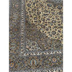 Central Persian Kashan pale khaki and ivory ground carpet, shaped central medallion enclosing small stylised motifs, the field decorated profusely with trailing foliate branches and plant motifs, guarded border with repeating floral design