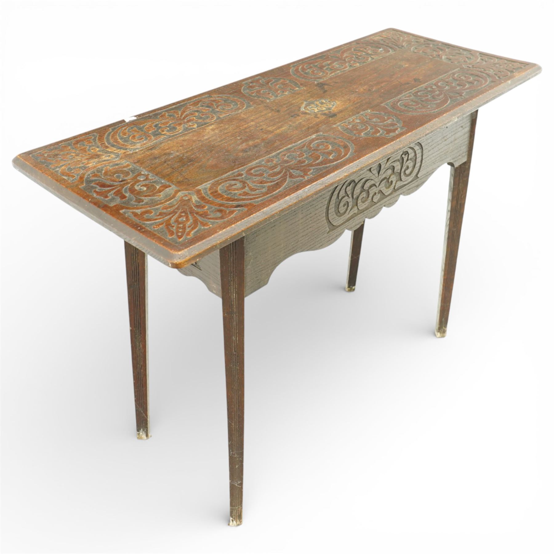 Arts and Crafts oak table, the rectangular top decorated with incised and carved scrolling foliage panels, the centre carved with a shield-shaped cartouche dated 1905, over a simple frieze with matching carved decoration to the front, on straight tapering legs