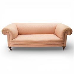 Victorian two seat sofa, upholstered in pink fabric, bowed form with scroll back and arms, raised on turned legs with castors