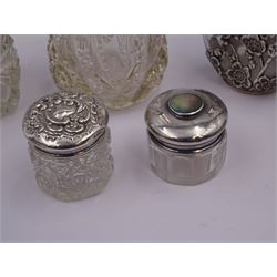 Two silver mounted dressing table jars, one in the form of a heart, both with embossed silver covers and cut glass bodies, hallmarked, together with two smaller examples, one set with mother of pearl, three silver mounted glass scent bottles, including an example with prunus blossom decoration, stamped Sterling, tallest bottle H17cm