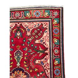 Persian Azerbaijan crimson ground rug, the field decorated with central floral motif and surrounded by trailing floral branches, enclosed within a shaped outer band with further floral decoration, the border with repeating flower heads, geometric guard stripes 