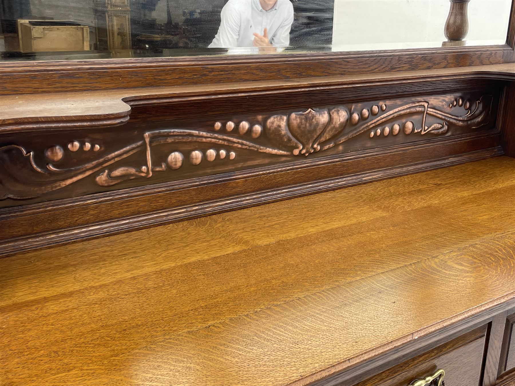 Arts and Crafts period oak mirror back dresser, projecting cornice above rectangular bevelled mirror and shelf, two turned supports, inset copper panel with embossed decoration, rectangular moulded top over two drawers and two panelled cupboard, moulded plinth base, brass and copper strappings and handles 
