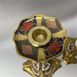 Pair of modern Royal Crown Derby Old Imari 1128 pattern candlesticks, each with shaped drip tray affixed to squat socket, upon spreading stem and canted square base with gilt dolphin edges, with printed marks beneath including Roman numeral year cypher for 2003, H26.5cm, with original boxes