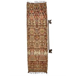 Ikat Man’s Cloth (Hinggi Kombu), East Sumba, Indonesia, woven in red, blue and yellow-brown warp ikat, constructed of two mirroring long panels, the motifs arranged in four bands depicting warrior figures astride rearing horses, high-ranking figures and guardians within geometric borders, on carved wooden wall hanger, L295cm
