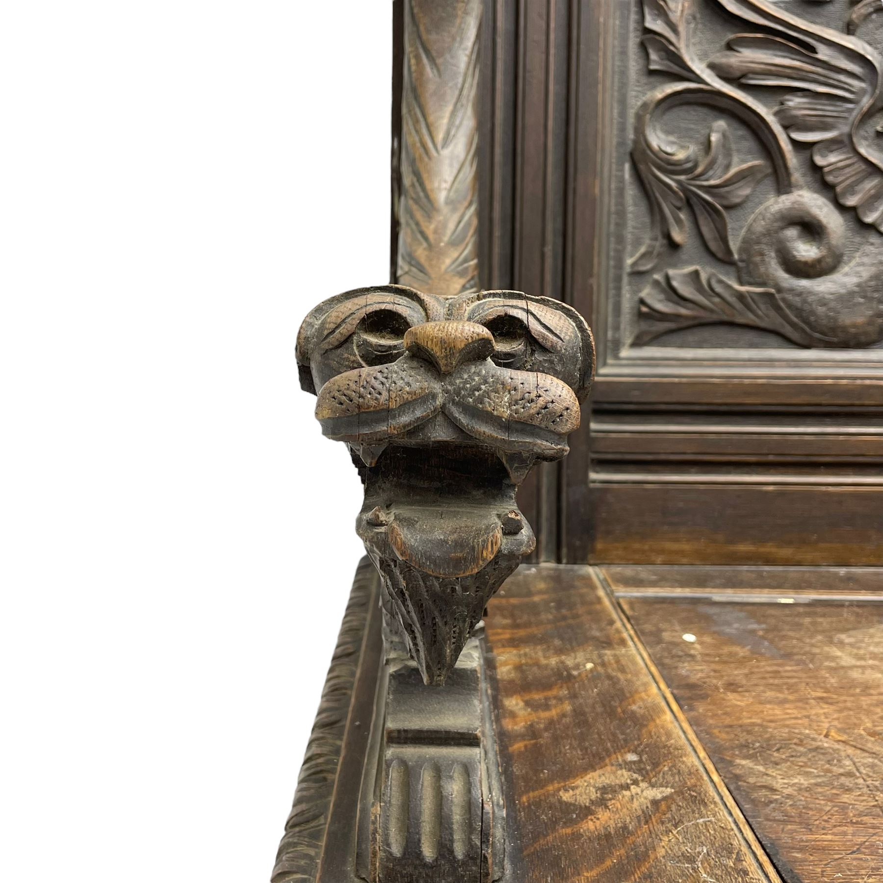 19th century oak hall bench, dentil cresting rail over moulded frame with panelled back carved with fire-breathing mythical beasts and central acanthus leaf motif, scroll carved down-sweeping arms carved with grotesque masks with scrolled foliage and shells, hinged box seat carved with scrolling foliage over panelled front with further carved foliage decoration, on paw carved front feet 