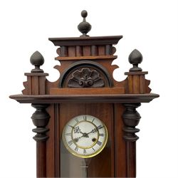 A late 19th century German wall clock with an 8-day spring driven movement striking the hours on a coiled gong, in a mahogany case with a shaped pediment and turned columns flanking a full-length glazed door, with a two-part dial enamel with Roman numerals, minute track and pierced gothic designed hands, gridiron pendulum and beat plate. With Key.




