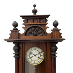 A late 19th century German wall clock with an 8-day spring driven movement striking the hours on a coiled gong, in a mahogany case with a shaped pediment and turned columns flanking a full-length glazed door, with a two-part dial enamel with Roman numerals, minute track and pierced gothic designed hands, gridiron pendulum and beat plate. With Key.




