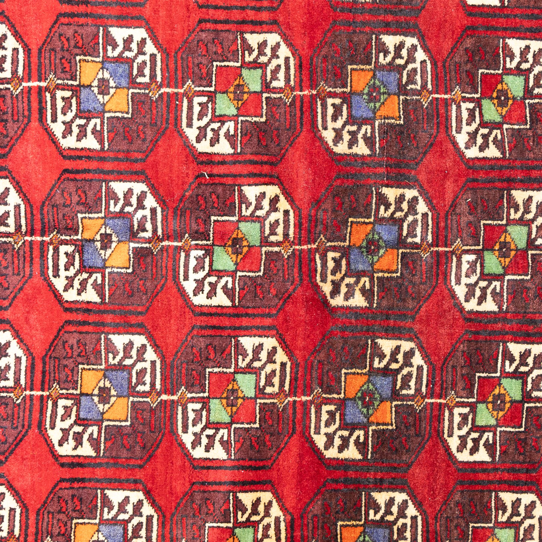 Tekke Bohara hand-knotted rug, madder red field decorated with an all-over design of repeating octagonal guls and latch-hook motifs within multiple geometric borders and cotton fringe ends 