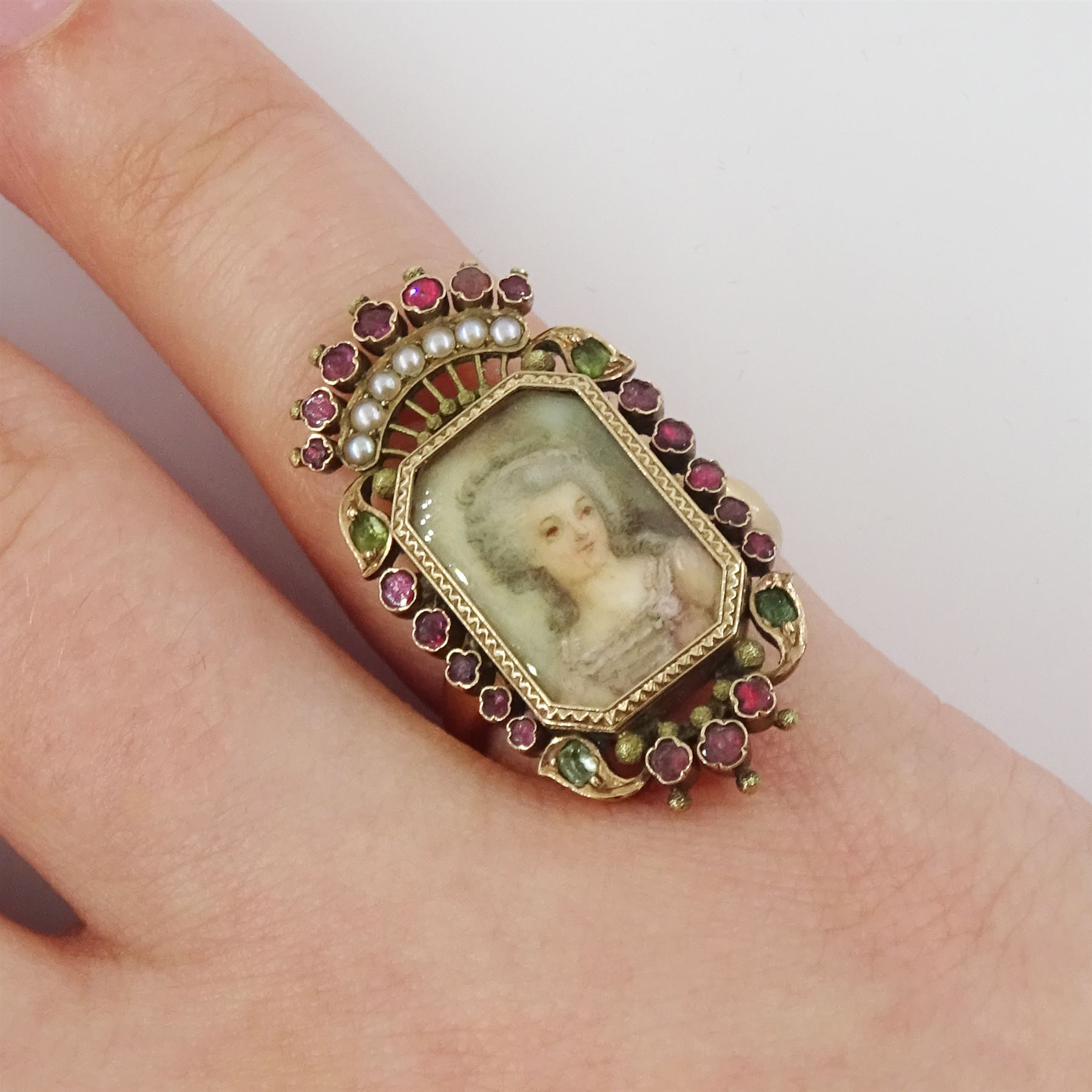 19th century 18ct gold portrait ring, set with an octagonal miniature of a woman wearing a pink dress on ivory, under a glazed panel, within a milled bezel and garnet surround, surmounted by a coronet set with seed pearls and further garnets. This lot has been registered for sale under Section 10 of the APHA Ivory Act