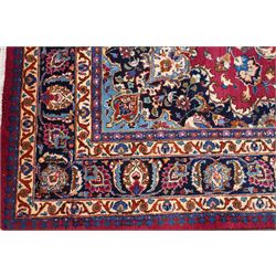 Central Persian Kashan hand-knotted carpet, rose red field, with central shaped lobed medallion issuing an all-over scrolling design of palmettes, floral sprays and arabesques, within conforming spandrels, enclosed by a broad indigo herati type palmette border framed by multiple guard stripes, in a palette of deep red, midnight blue and ivory tones, with cotton fringe ends, and Kashan signature 
